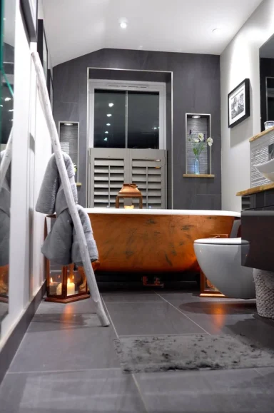 Modern bathroom featuring a copper freestanding bathtub, grey tiles, and stylish decor.