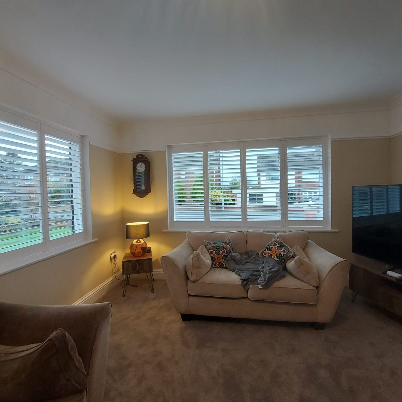 Cozy living room with large windows, a sofa, armchair, and a television.