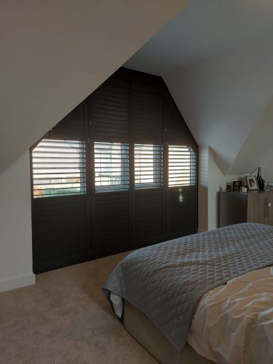 A cosy bedroom with a sloped ceiling, featuring a bed and window shutters.