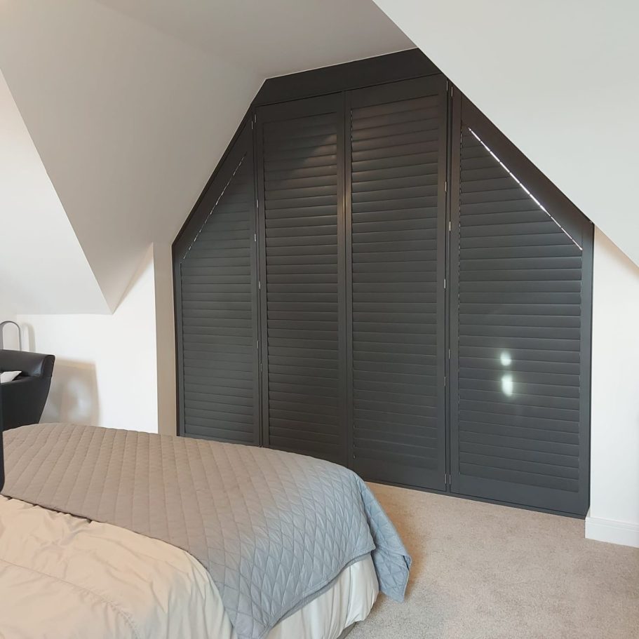 A modern bedroom with a sloped ceiling and grey shutters on the wall.