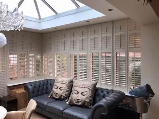 A stylish living room with a black leather sofa, Buddha cushions, and wooden shutters.