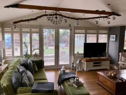 Living room with green sofas, a wooden beam, large windows, and a television unit.