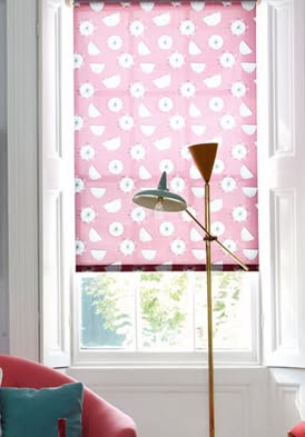 A pink roller blind with a floral pattern in a well-lit room.