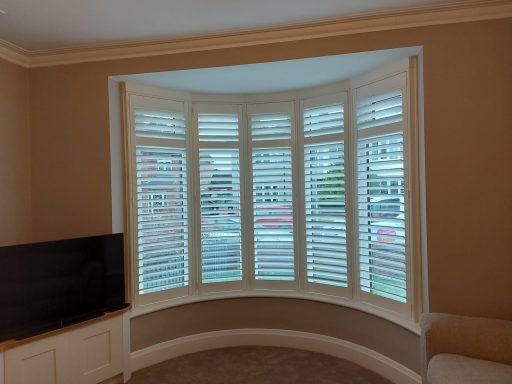 Bay window with shutters, cream walls, and a corner television unit.