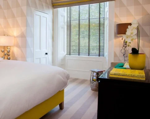 Brightly lit bedroom featuring a large bed, side table, and decorative window.