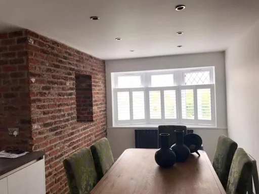 Modern dining room with a wooden table, green chairs, and exposed brick wall.