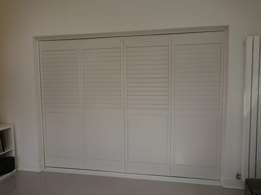 White louvred shutters closed over a wide window or wall space.