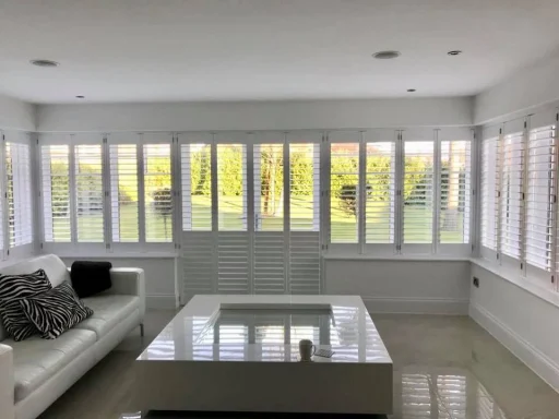 Bright living room with a white sofa, coffee table, and large windows overlooking a garden.
