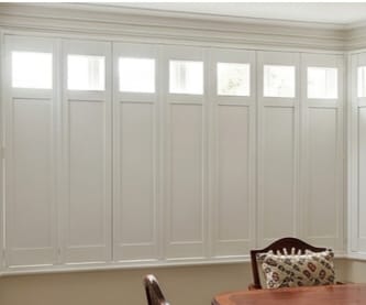 White wooden window shutters with small upper panes, above a wooden dining table.