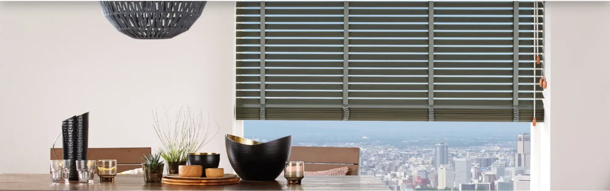 Blinds covering a large window overlooking a cityscape, with dining area in foreground.