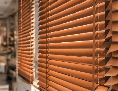 Brown wooden blinds partially closed against a bright interior backdrop.
