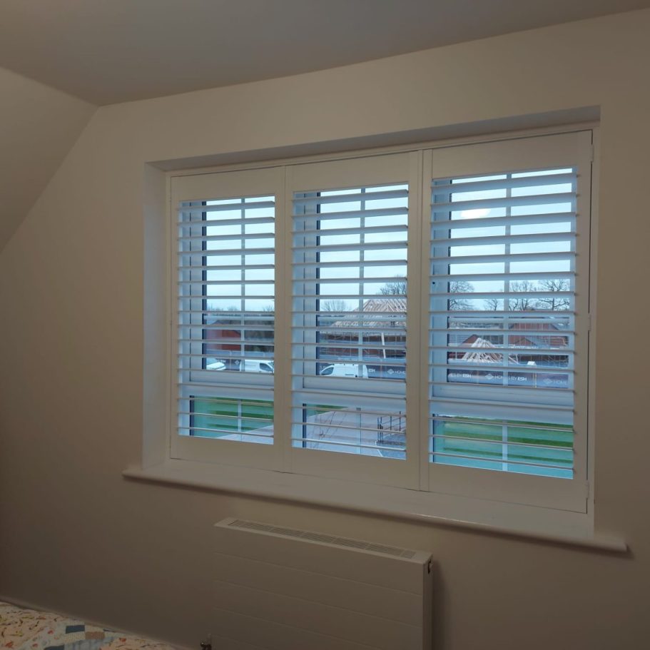 Made-to-measure plantation shutters installed in a modern Middlesbrough living room. A window with white shutters overlooking a green lawn and buildings outside.