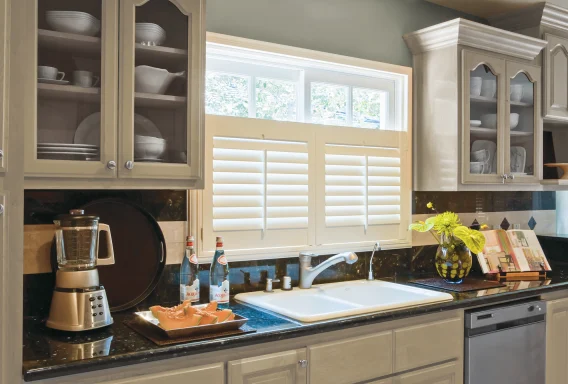 Modern kitchen with beige cabinets, black countertops, and a window featuring wooden blinds.