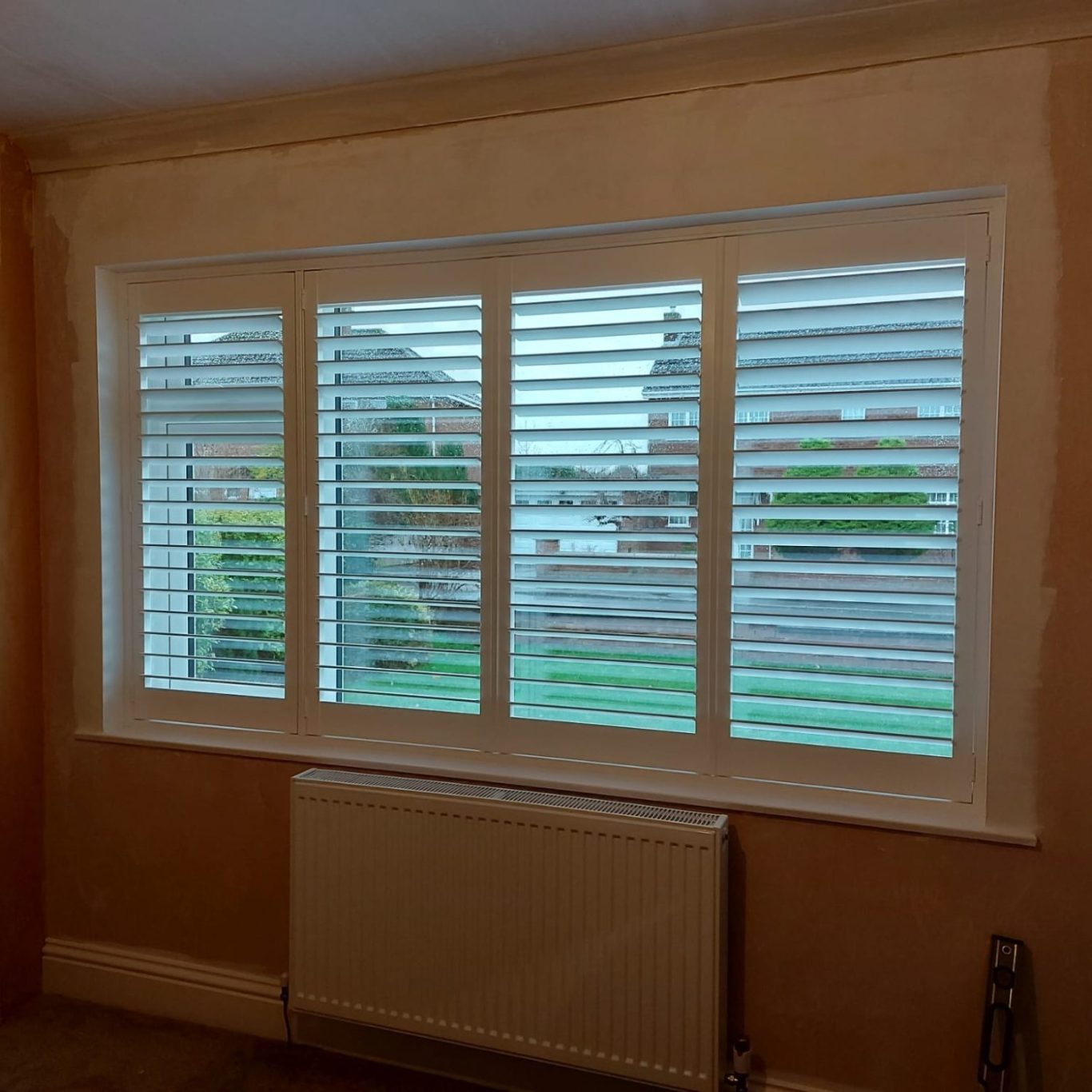 Window with horizontal blinds overlooking a garden, featuring light-coloured walls.