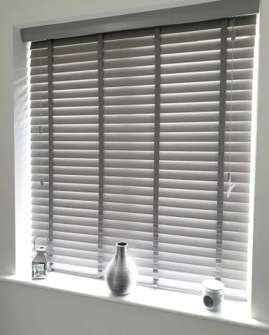 A window with grey blinds, decorated with two vases on a ledge.