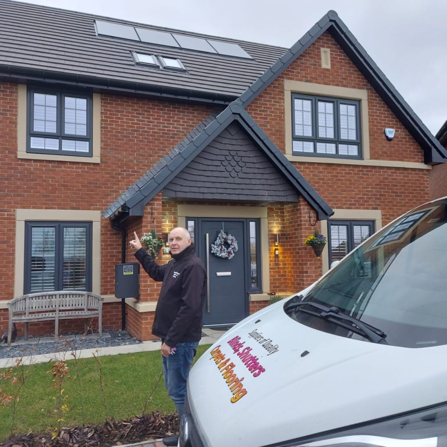 A man stands outside a modern brick house, pointing at the entrance. A van is parked nearby.