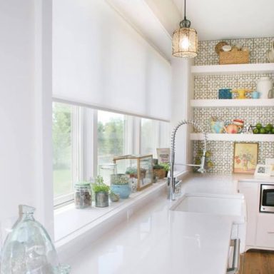 Bright modern kitchen with white countertops, shelves filled with dishware, and natural light.