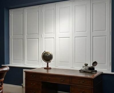 A wooden desk with a globe, beside a window featuring white shutters against blue walls.